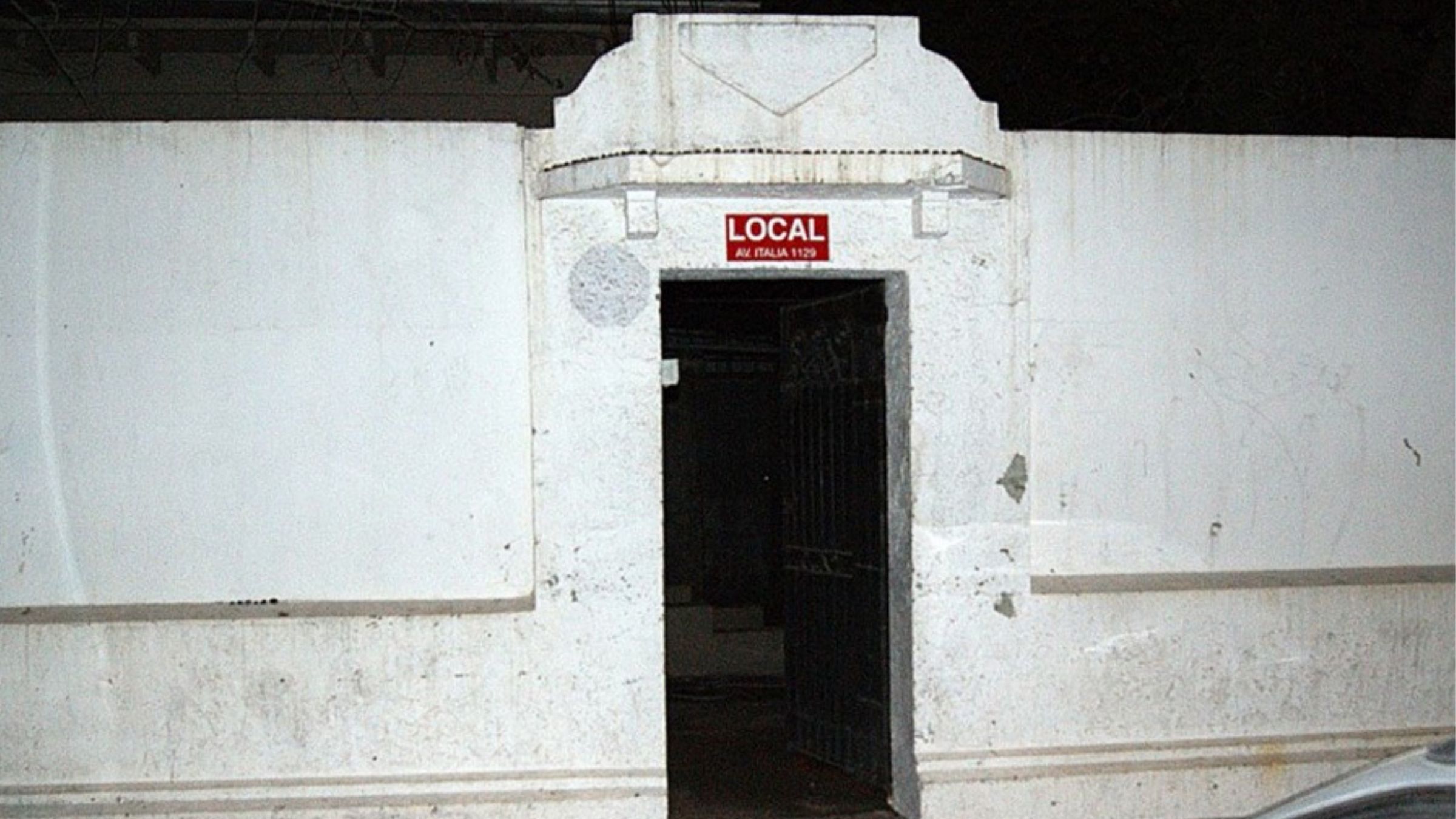 Página 3 de 19. Fachada blanca de LOCAL con su letrero rojo sobre la puerta