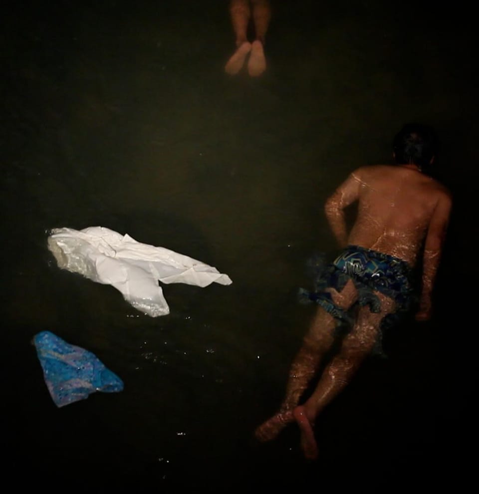 Visitante nadando boca abajo en el agua oscura junto a telas flotantes, los pies de otra persona al fondo